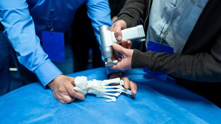 Medical Device Development | Manar, Inc. | Manar, Inc. Medical professionals use a handheld instrument on a white foot skeleton model on a blue table cover during training.