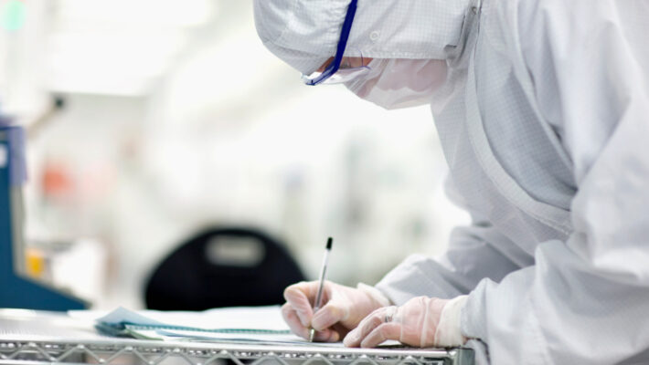 Controlled Environment | Manar, Inc. | Manar, Inc. Scientist in protective gear writing on a clipboard in a laboratory setting